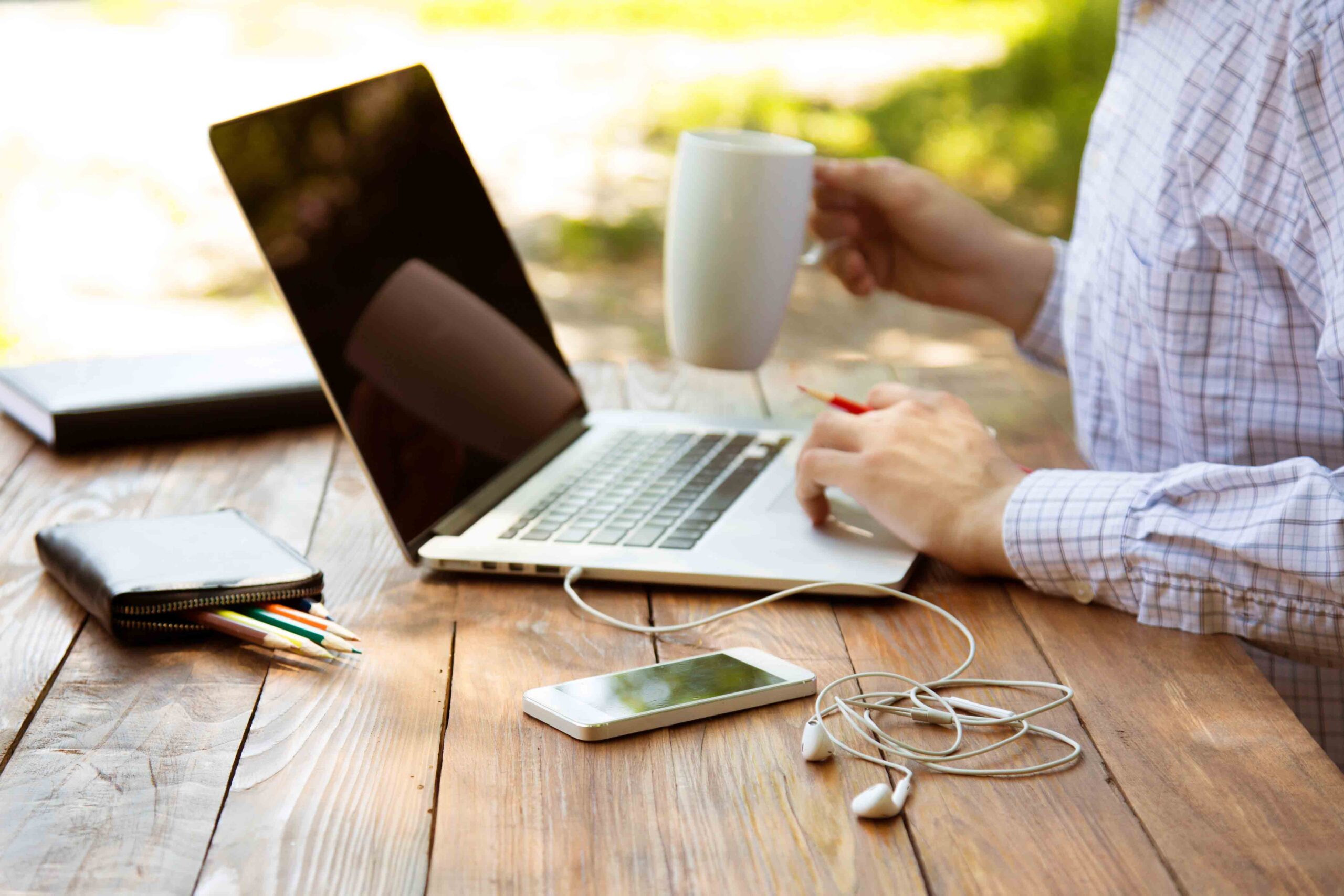 Person sitting at table working on laptop while drinking coffee