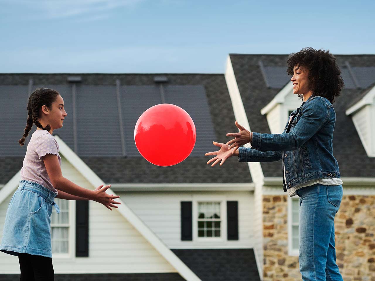 Mother and daughter playing ball outside their home.